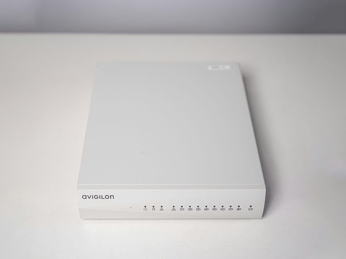 Weißes elektronisches Gerät auf hellem Tisch mit Avigilon-Logo und LEDs.