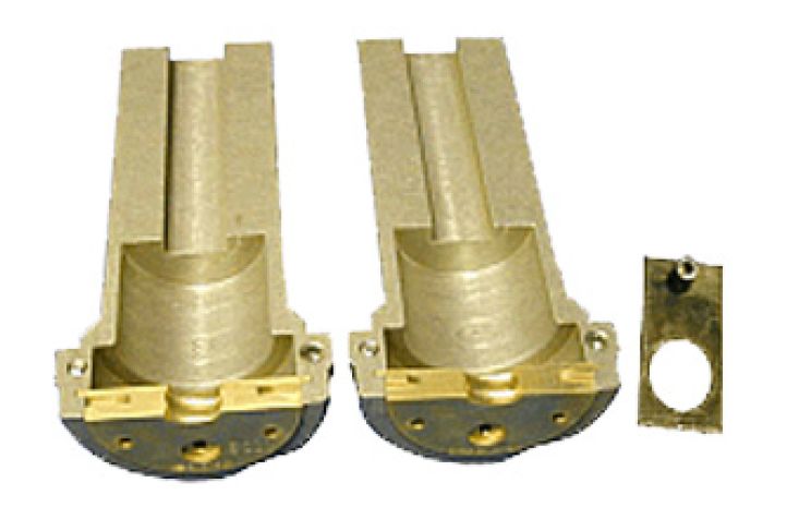 Zwei goldene Metallzylinder mit rechteckigem Sockel, daneben rechteckige Metallplatte mit Loch.