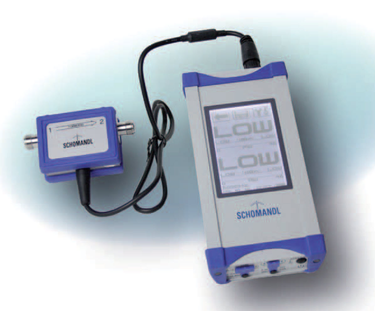 Messgerät mit Bildschirm, verbunden mit einem kleinen, blauen Adapter, beide mit SCHOMANDL beschriftet.