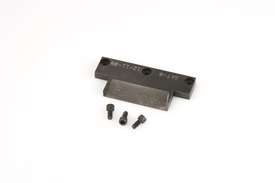 Schwarzes Metallteil mit drei kleinen Schrauben auf weißem Hintergrund.