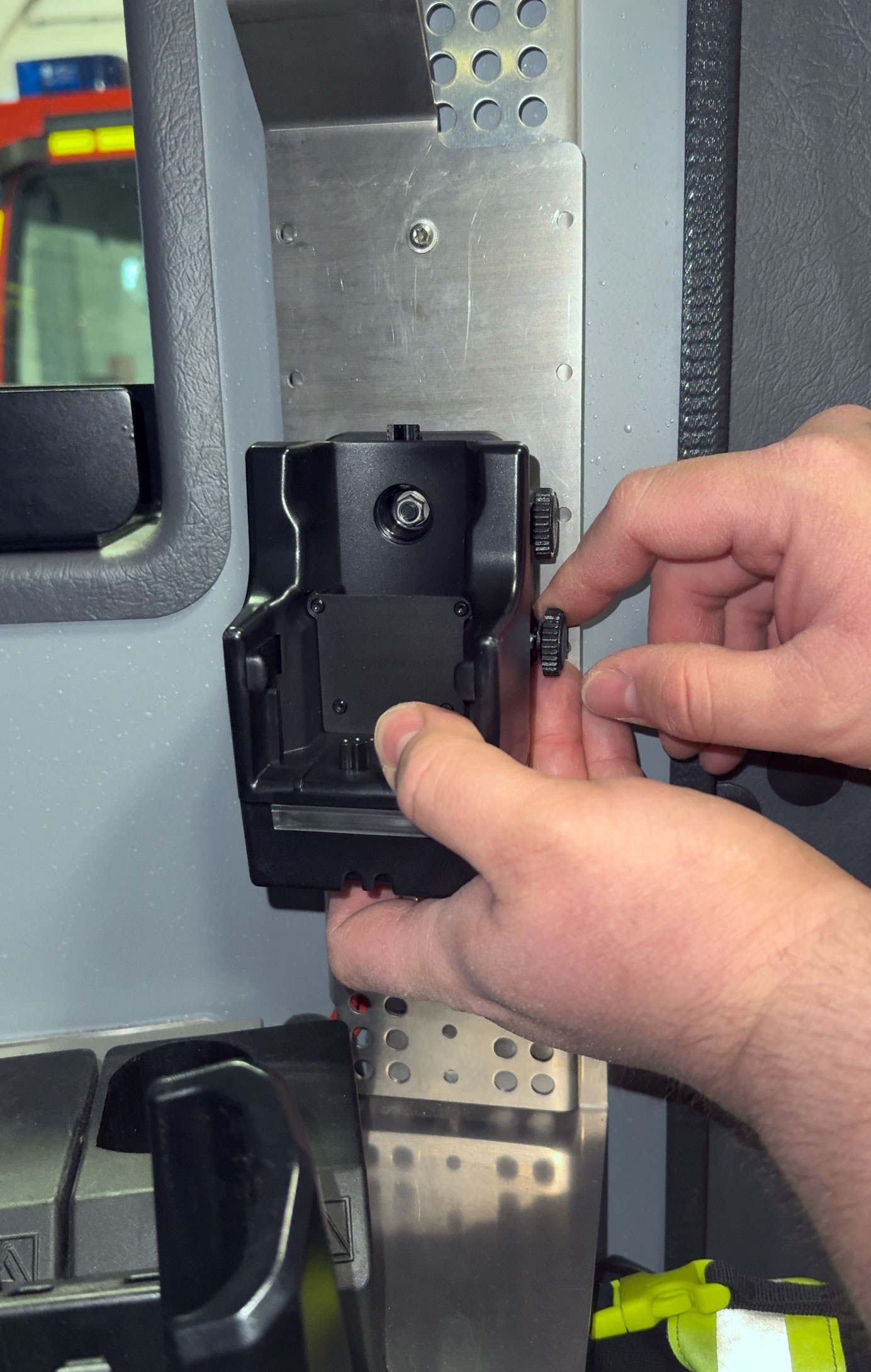 Hands adjusting a black electronic device on a metal plate indoors.