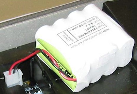 Weiße Batterie im Batteriefach mit grünen Zellen und roten Kabeln.