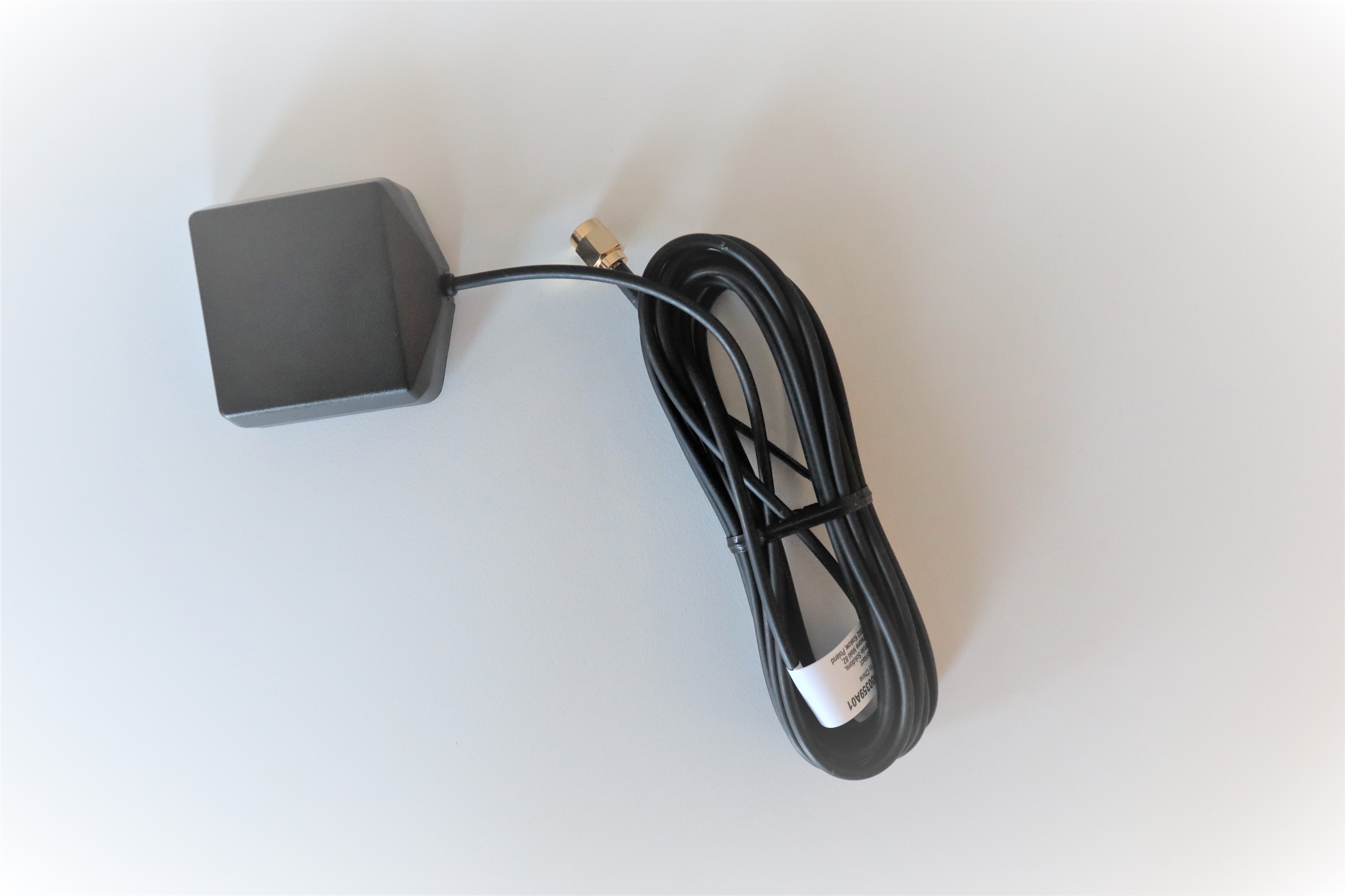 7000-00750598_mot_01.jpg Schwarze quadratische GPS-Antenne mit langem Kabel auf weißem Hintergrund.