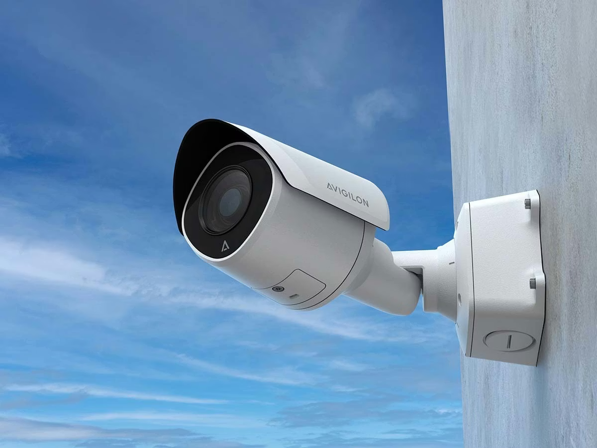 An Wand montierte Überwachungskamera vor blauem Himmel.