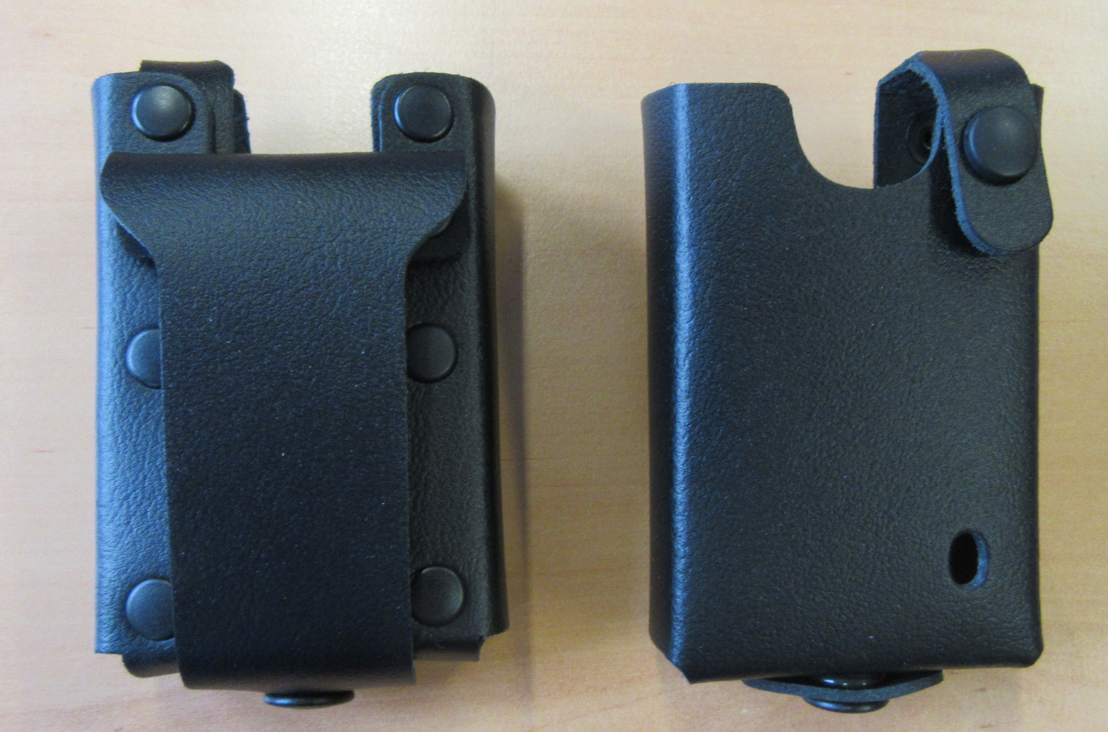Two black leather cases with snap closures on a wooden surface.